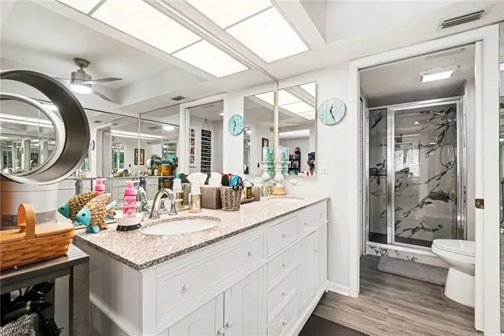 Bathroom featuring double vanity, a marble finish shower, light wood-style flooring, and a ceiling fan