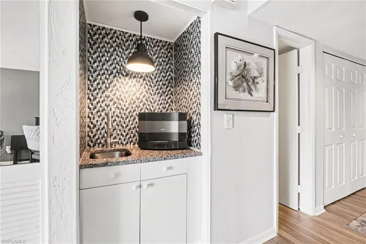 decorative backsplash, white cabinetry, light stone countertops, pendant lighting, and light tile/wood-type flooring