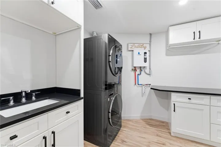 Laundry room featuring cabinet space, light wood-style flooring, stacked washer and clothes dryer, and water heater
