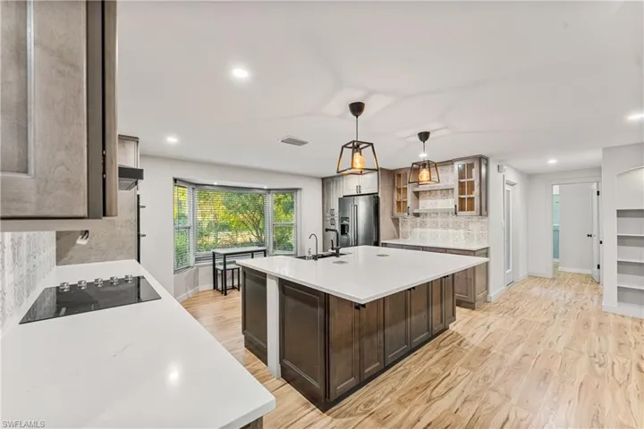 Kitchen featuring backsplash, an island with sink, light wood finished floors, decorative light fixtures, and dual tone cabinets