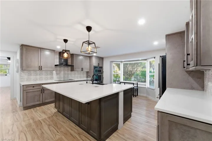 Kitchen with pendant lighting, a center island with sink, light wood-style flooring, light stone countertops, and dark wood finish cabinets