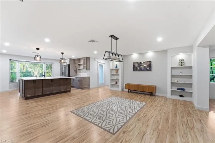 Kitchen with dark wood finish cabinets, a kitchen island with sink, pendant lighting, light wood-style floors, and open floor plan