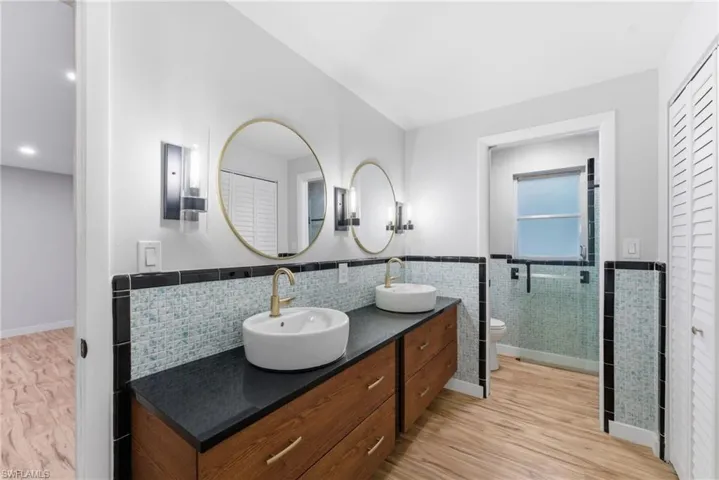 Bathroom featuring a closet, double vanity, light wood-type flooring, tile walls, and a wainscoted wall