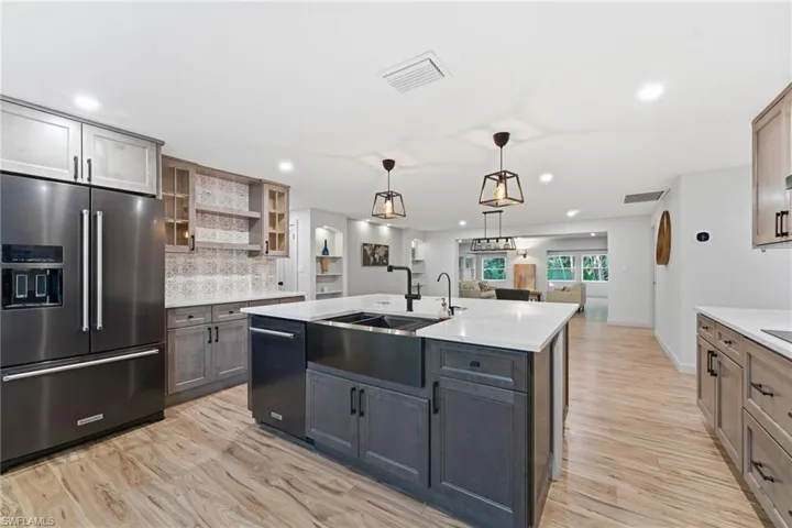 Dual tone kitchen featuring high end refrigerator, open shelves, a center island with sink, light wood-style floors, and two tone color scheme