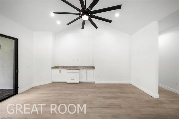 Unfurnished room with light hardwood / wood-style flooring, built in desk, ceiling fan, and vaulted ceiling