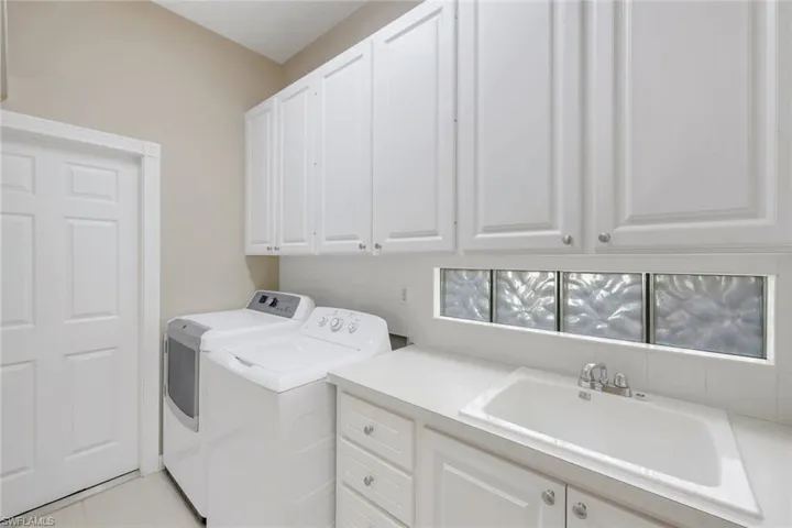 White cabinetry with silver-tone hardware, a utility sink with a chrome faucet, a white countertop, and glass block window accents