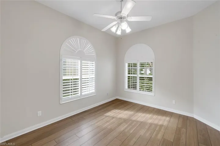 Vaulted ceiling, wood-finish flooring, two arched windows, built-in plantation shutters, and ceiling fan with integrated lighting
