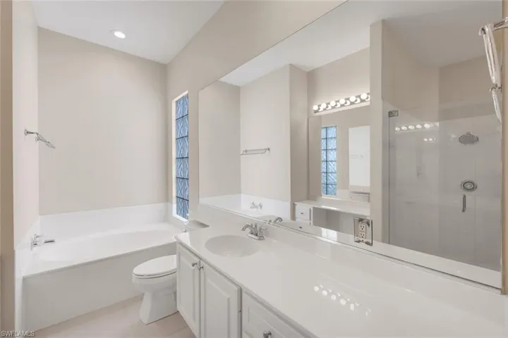 Bathroom featuring a soaking tub, glass-enclosed shower, dual vanity with white cabinetry, and a full-width mirror