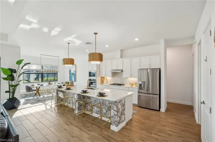 Kitchen featuring a breakfast bar area, hanging light fixtures, an island with sink, stainless steel appliances, and white cabinets