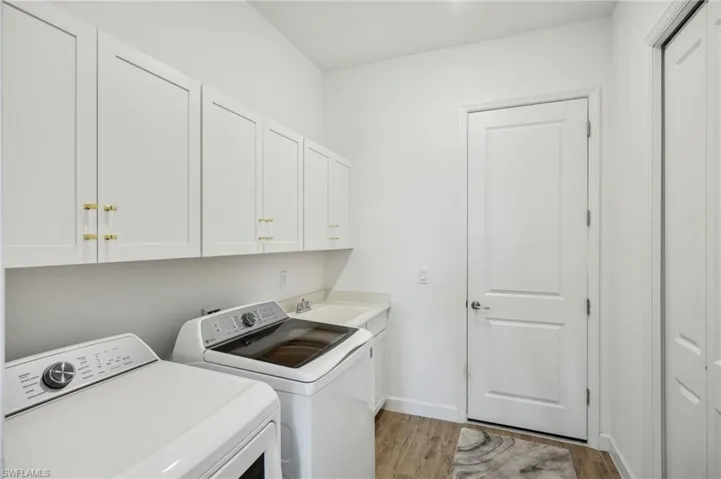 Washroom featuring cabinets, washing machine and clothes dryer, sink, and light wood-type flooring