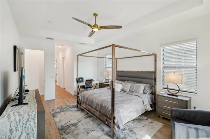 Bedroom featuring ceiling fan, a tray ceiling, light hardwood / wood-style floors, and a closet