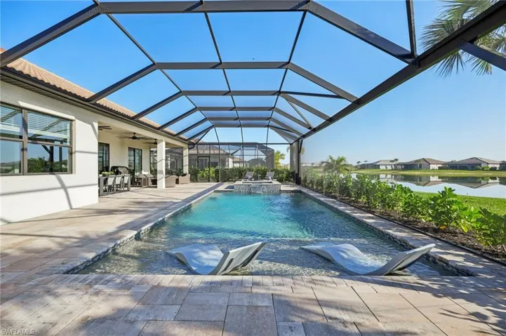 View of swimming pool featuring an in ground hot tub, a lanai, ceiling fan, a water view, and a patio area