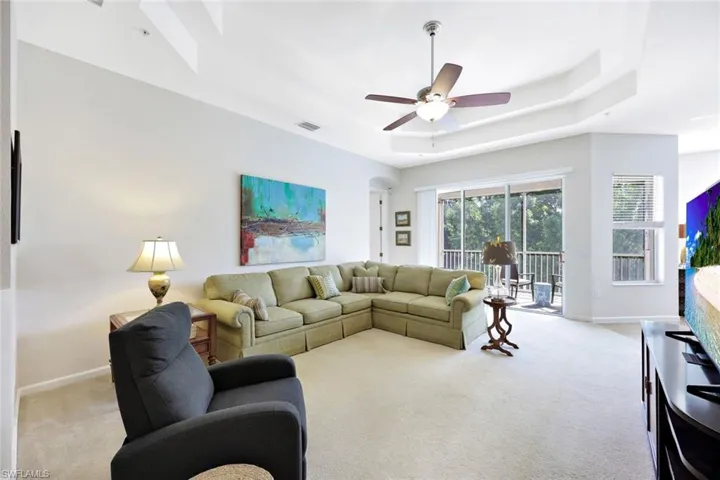 Carpeted living area featuring a ceiling fan and a tray ceiling
