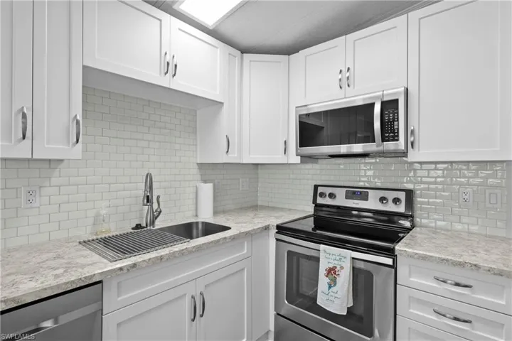 Kitchen featuring light stone countertops, stainless steel appliances, white cabinets, backsplash, and sink
