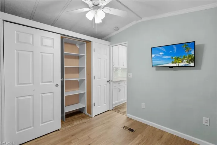 Unfurnished bedroom with ceiling fan, ornamental molding, light hardwood / wood-style floors, and lofted ceiling