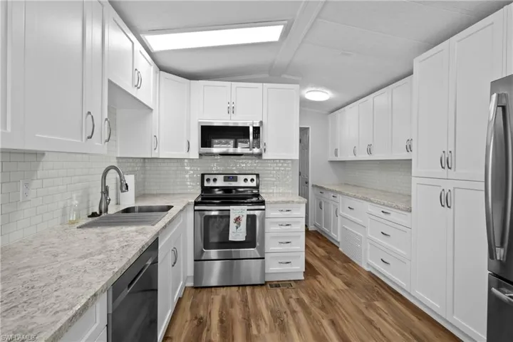 Kitchen with stainless steel appliances, lofted ceiling, backsplash, and dark wood-type flooring