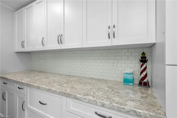 Kitchen featuring light stone counters, white cabinetry, ornamental molding, and tasteful backsplash