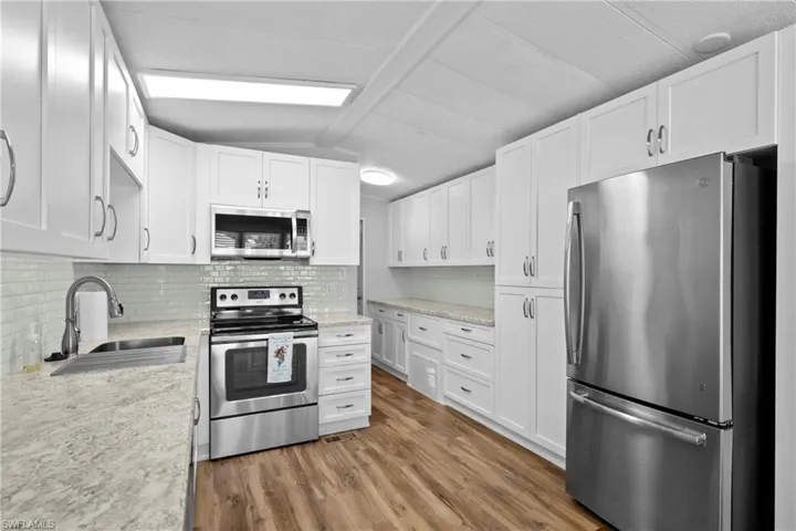 Kitchen with stainless steel appliances, hardwood / wood-style floors, sink, tasteful backsplash, and vaulted ceiling