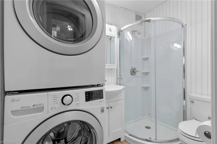 Bathroom with a shower with shower door, stacked washer and dryer, and toilet
