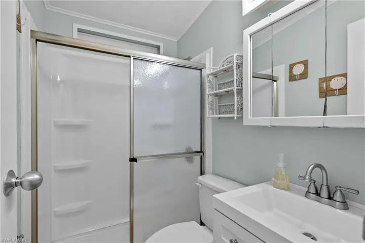 Bathroom with ornamental molding, toilet, vanity, and a shower with door