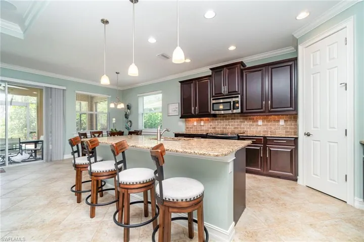 Kitchen featuring stainless steel microwave, decorative backsplash, a breakfast bar, light stone counters, and a center island with sink