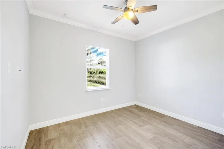 Empty room featuring crown molding, light wood-style floors, and ceiling fan
