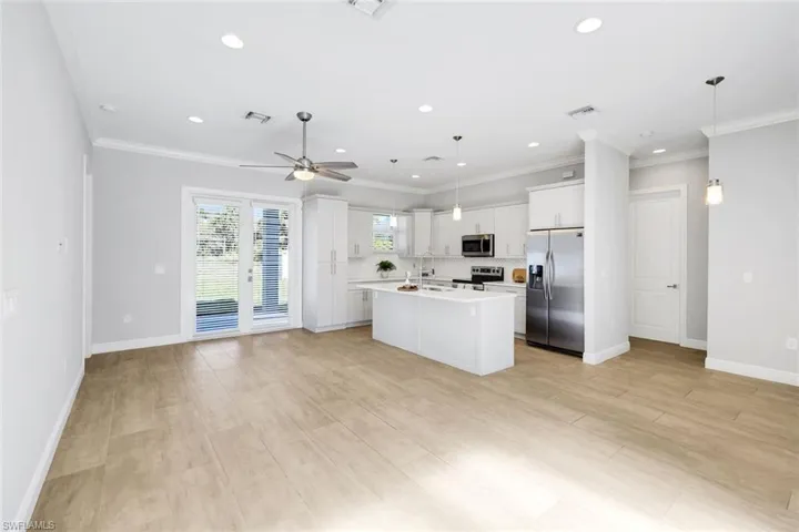 Kitchen with light countertops, stainless steel appliances, pendant lighting, a center island with sink, and white cabinets