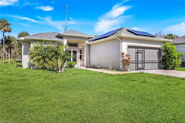 View of front facade with a front lawn, stucco siding, driveway, and solar panels