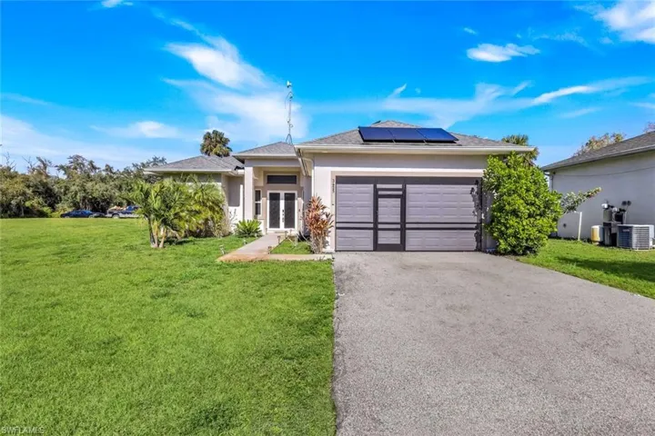 View of front of property featuring a front lawn, asphalt driveway, roof mounted solar panels, stucco siding, and an attached garage