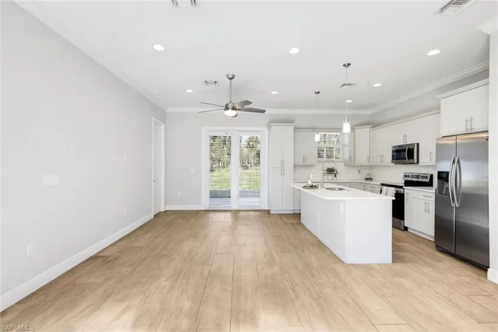 Kitchen with appliances with stainless steel finishes, a center island with sink, white cabinetry, crown molding, and hanging light fixtures
