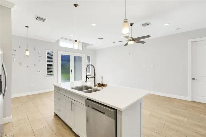 Kitchen featuring white cabinetry, stainless steel appliances, crown molding, decorative light fixtures, and an island with sink