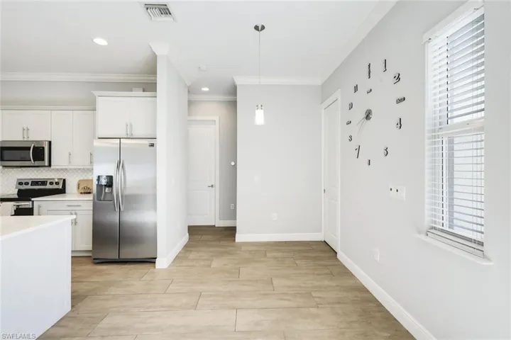 Kitchen featuring appliances with stainless steel finishes, white cabinetry, backsplash, decorative light fixtures, and crown molding