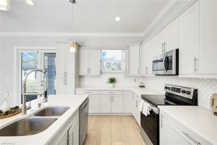 Kitchen featuring stainless steel appliances, white cabinets, decorative light fixtures, crown molding, and light stone countertops