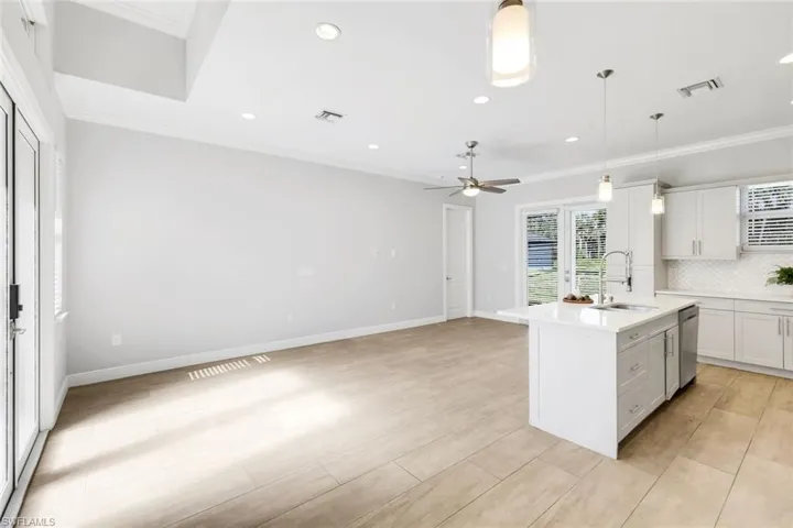 Kitchen featuring white cabinets, an island with sink, ornamental molding, decorative backsplash, and open floor plan