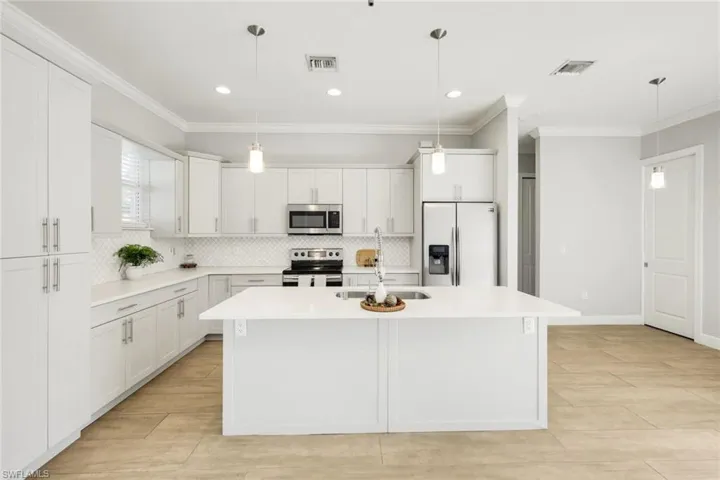 Kitchen featuring crown molding, appliances with stainless steel finishes, backsplash, white cabinetry, and pendant lighting
