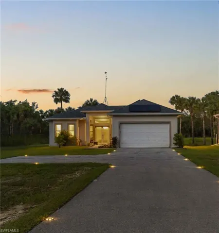 Ranch-style house featuring asphalt driveway, a lawn, solar panels, stucco siding, and an attached garage