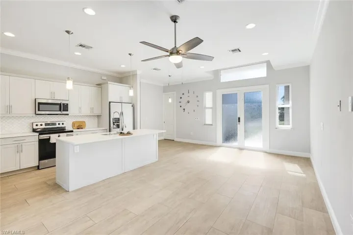 Kitchen with open floor plan, stainless steel appliances, decorative light fixtures, a center island with sink, and backsplash