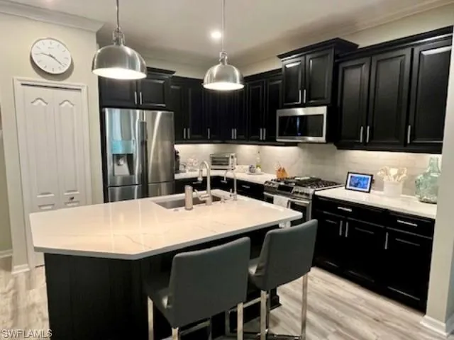 Kitchen with dark cabinets, appliances with stainless steel finishes, crown molding, and decorative backsplash