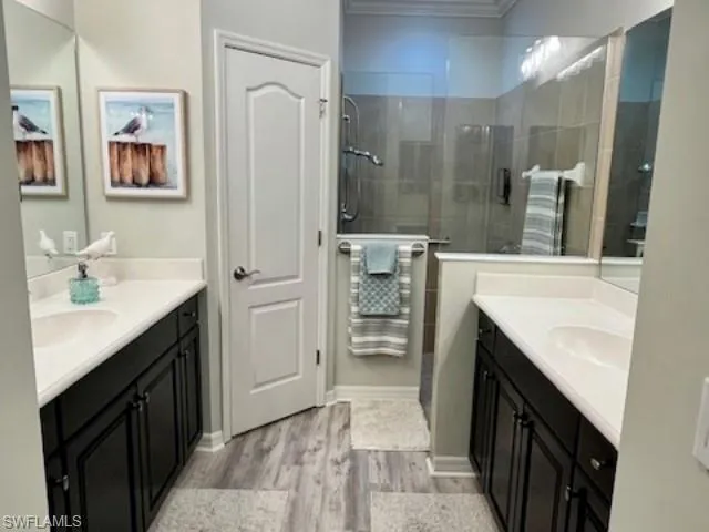 Full bath with two vanities, wood finished floors, a shower stall, and ornamental molding
