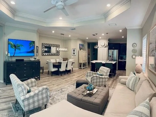 Living room featuring a tray ceiling, light wood-type flooring, a ceiling fan, crown molding, and recessed lighting