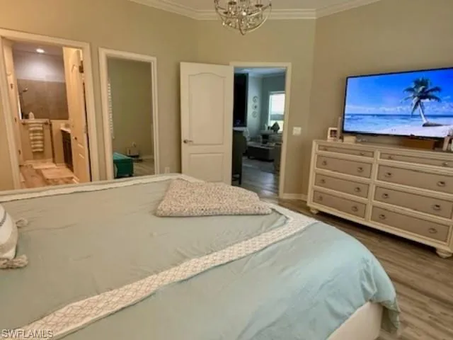 Bedroom featuring crown molding, wood finished floors, a chandelier, and ensuite bath