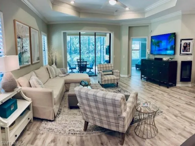 Living area featuring a raised ceiling, light wood-style floors, ornamental molding, and a ceiling fan
