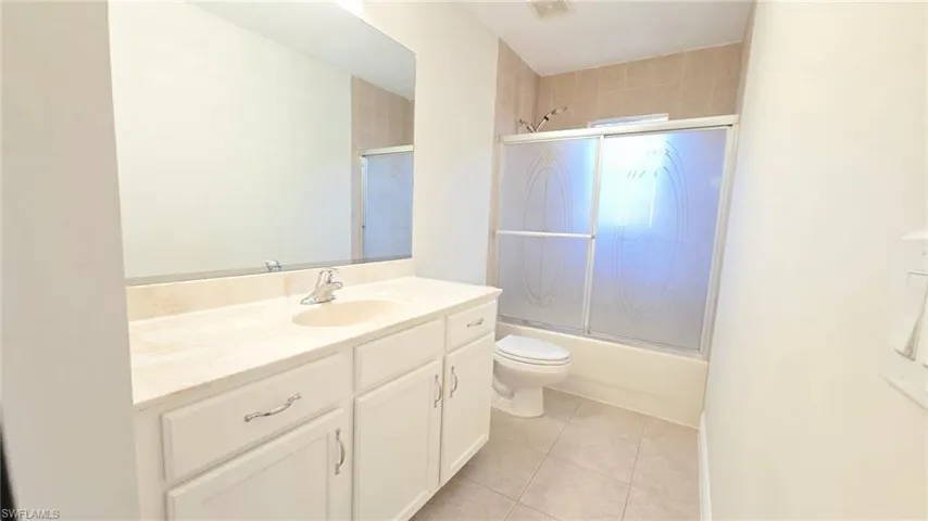 Bathroom featuring combined bath / shower with glass door, tile patterned floors, toilet, vanity, and visible vents