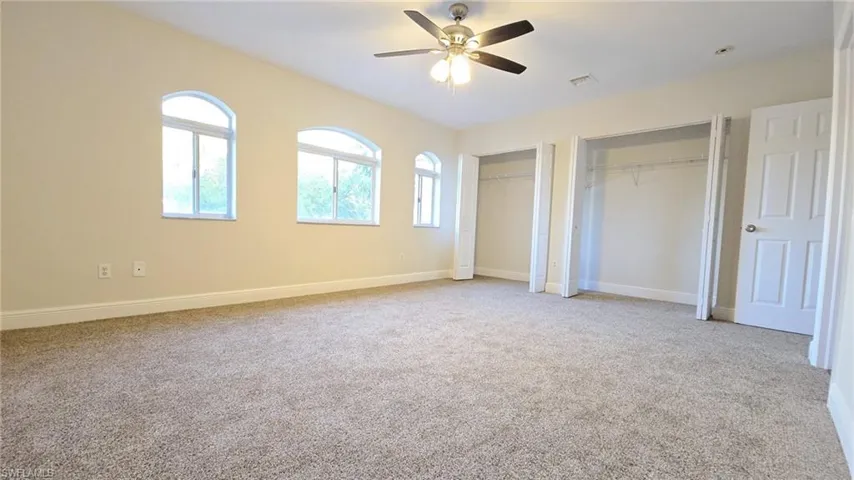 Unfurnished bedroom featuring baseboards, multiple closets, carpet floors, visible vents, and ceiling fan