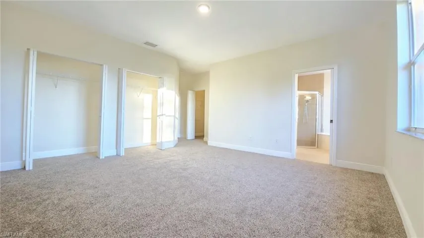 Unfurnished bedroom featuring light carpet, baseboards, multiple closets, and connected bathroom