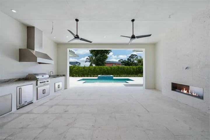 The outdoor covered living space provides ample space for comfy socializing, with a natural gas fireplace and full outdoor kitchen with gas grill, sink, under counter fridge, and storage. The covered living opening has been pre-wired for optional motorized roll down bug/storm screens.