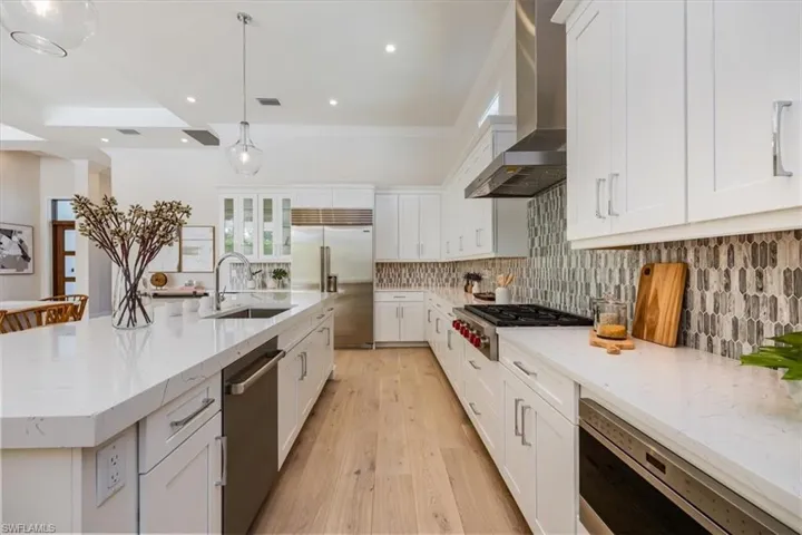 The open concept main living area features a vaulted ceiling with nickel gap and beam work, 10' impact pocket sliders, and Sub-Zero/Wolf kitchen appliance suite