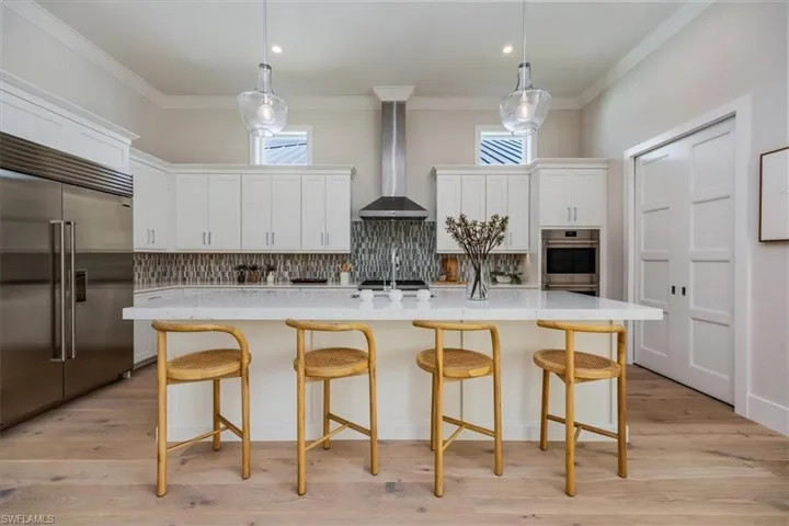 The open concept main living area features a vaulted ceiling with nickel gap and beam work, 10' impact pocket sliders, and Sub-Zero/Wolf kitchen appliance suite