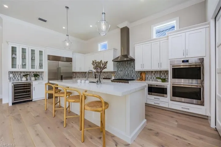 The open concept main living area features a vaulted ceiling with nickel gap and beam work, 10' impact pocket sliders, and Sub-Zero/Wolf kitchen appliance suite