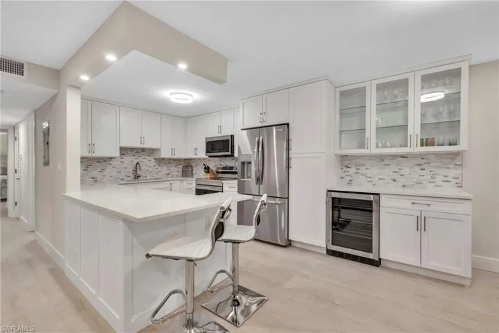 Kitchen featuring wine cooler, stainless steel appliances, white cabinets, glass fronted cabinets, and a peninsula